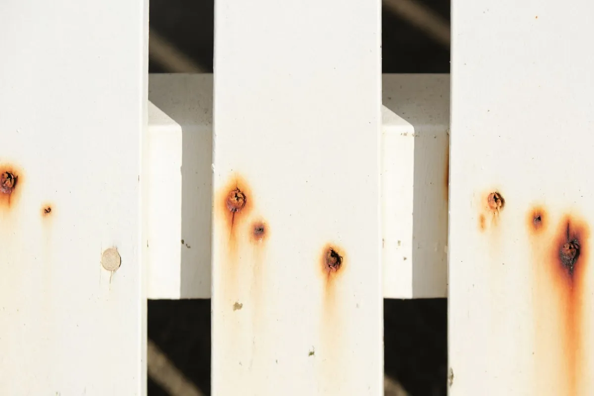 Close-up of a white painted surface with multiple rust spots forming around old screw holes.